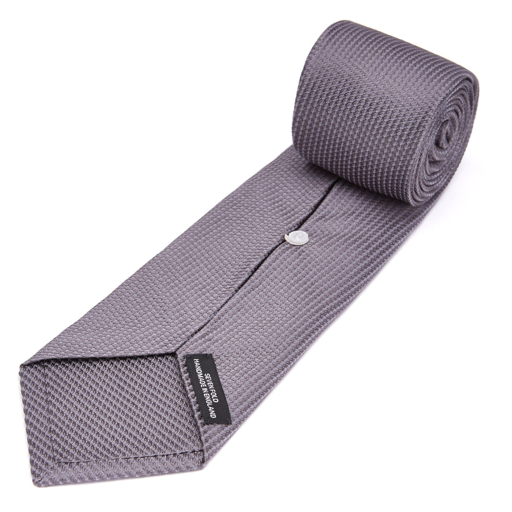 A close-up of the Dark Grey Plain Woven Lace Silk Tie by Turnbull & Asser, neatly rolled and textured, displayed on a light background—an elegant accessory for smart wardrobes.