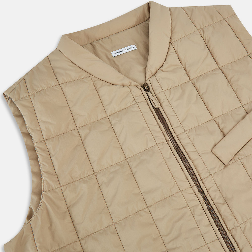 The Turnbull & Asser Sand Quilted Gilet is a beige, lightweight vest featuring a front zipper, two zippered side pockets, a chest pocket, and a rounded hem, shown against a white background.