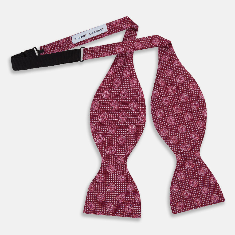 The Turnbull & Asser Burgundy Medallion Silk Bow Tie, featuring small white circles and crosshatch lines, is displayed on a plain white background—perfect for adding sophistication to smart attire.