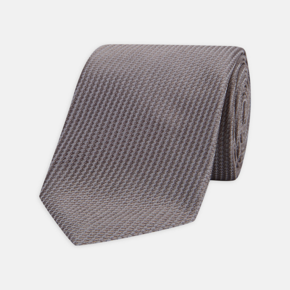 A close-up of the Dark Grey Plain Woven Lace Silk Tie by Turnbull & Asser, neatly rolled and textured, displayed on a light background—an elegant accessory for smart wardrobes.