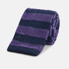 View 1 of product The KNITTED STRIPE PURPLE TIE by Turnbull & Asser features bold dark blue and purple stripes, making it an essential smart accessory. Shown rolled up on a white background.