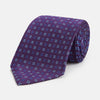 View 1 of product The Turnbull & Asser MINI SQUARE SPOT PLUM BLUE TIE is a luxury English silk necktie in plum, featuring a blue and white grid pattern of small squares, displayed rolled up against a simple light background.