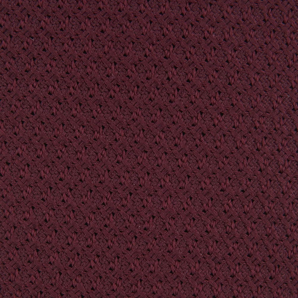 The Turnbull & Asser 7 fold Grenadine Silk Plain Tie is shown rolled on a white background, highlighting its textured maroon design as a versatile addition to any wardrobe.