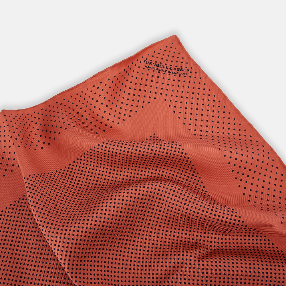 The Orange Dot Silk Pocket Square by Turnbull & Asser is handmade in England from silk, featuring small black polka dots and a solid orange border with a folded corner.