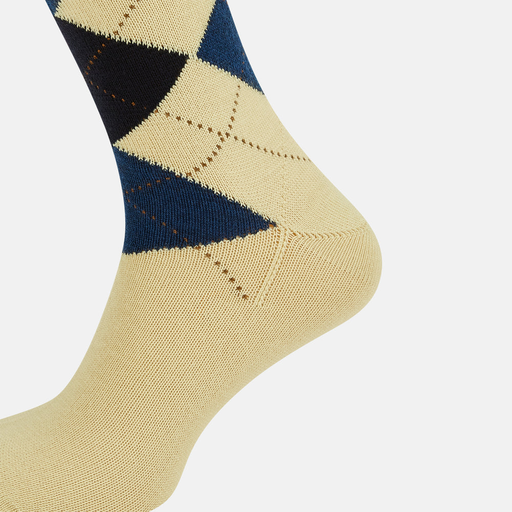 The Turnbull & Asser Vanilla Wool Check Mid-Length Sock is beige with blue, black, and white argyle diamonds on the side and solid beige toe, heel, and cuff. Displayed on a plain white background.