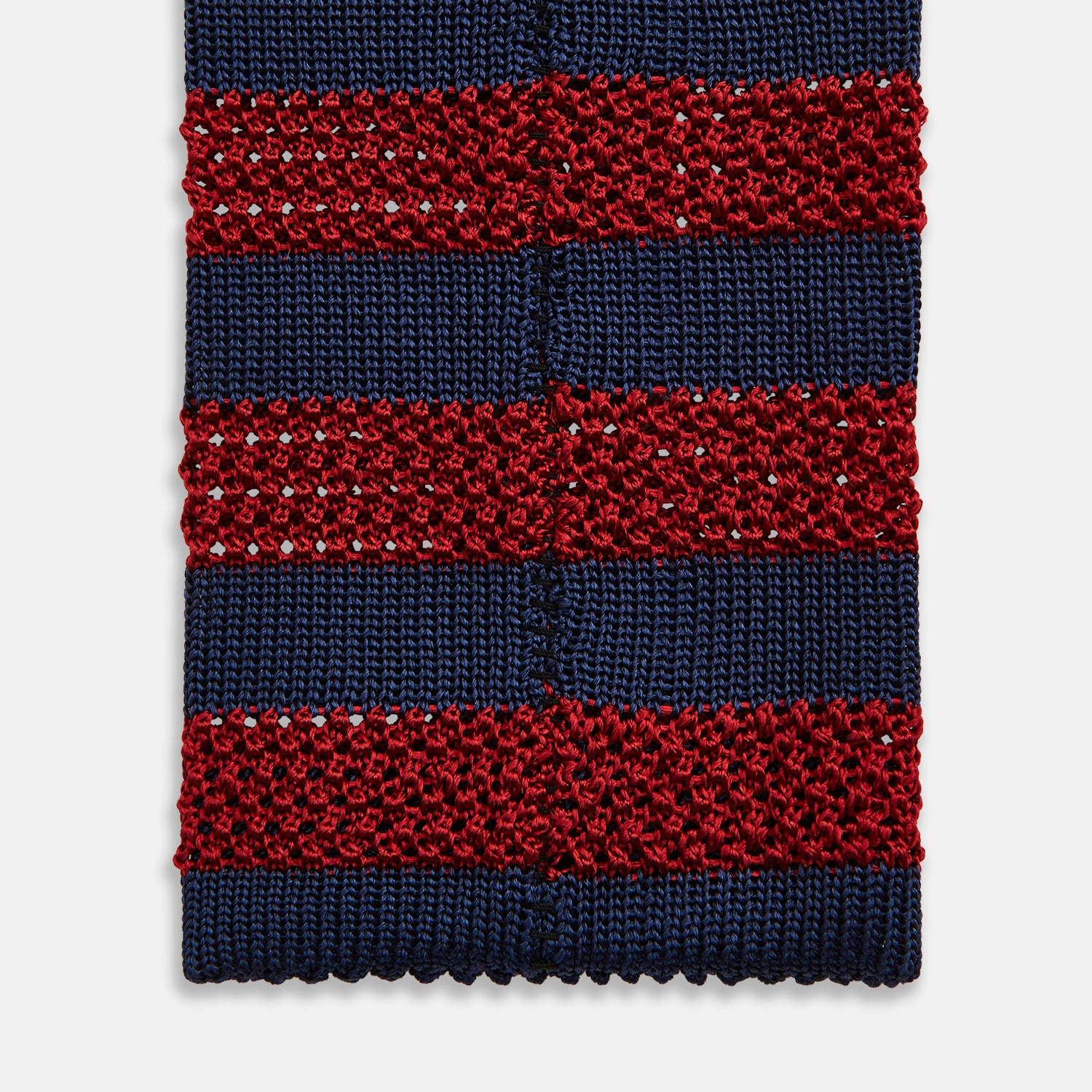 View 4 of product The Turnbull & Asser KNITTED STRIPE RED TIE features bold red and navy wide stripes in a rolled-up, knitted design—an eye-catching accessory shown on a plain white background.