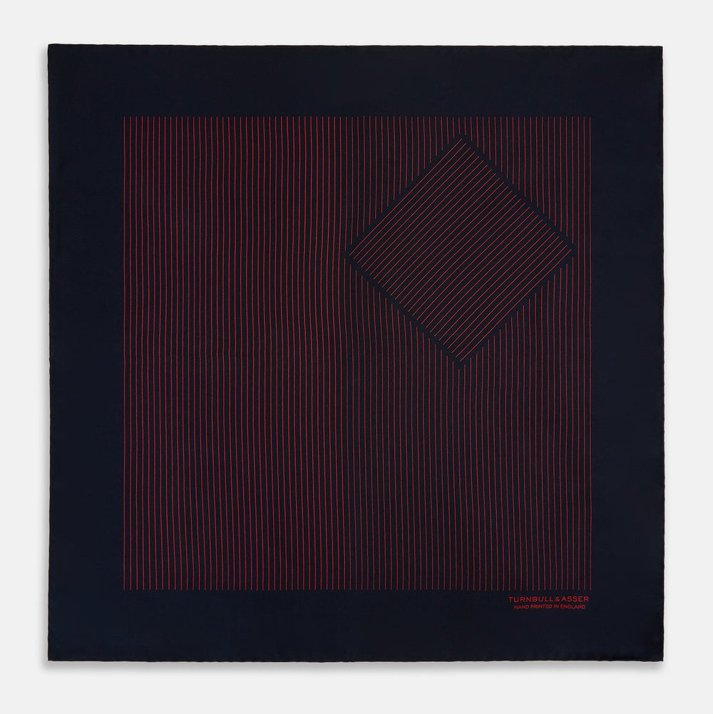 The Turnbull & Asser Navy and Red Stripe Silk Pocket Square features thin red stripes on navy silk, with "HAND PRINTED IN ENGLAND" in red at the corner. A folded corner shows its hand-rolled edges and refined design.
