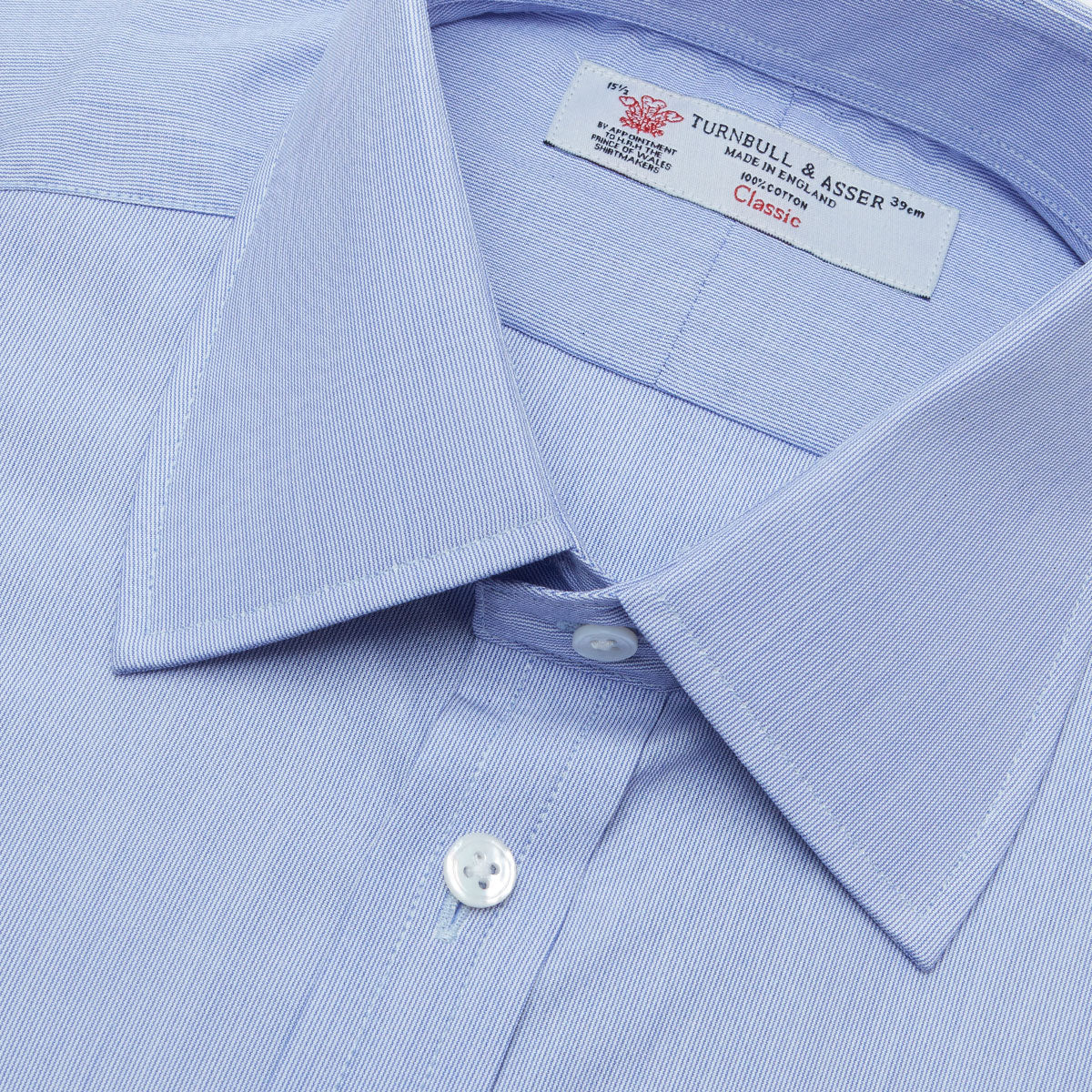 View 5 of product The Turnbull & Asser Blue Hairline Stripe Shirt features a T&A collar, 3-button cuffs, and white buttons. Made from light blue cotton with subtle stripes, it’s neatly folded with the label visible inside the collar on a plain white background.