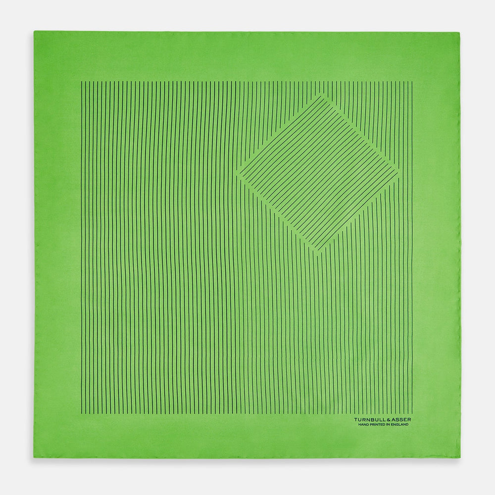 The Fern Green Stripe Silk Pocket Square by Turnbull & Asser features thin black vertical stripes, celebrates British heritage, and is inscribed “TURNBULL & ASSER HAND PRINTED IN ENGLAND” in one corner; one corner is folded inward.