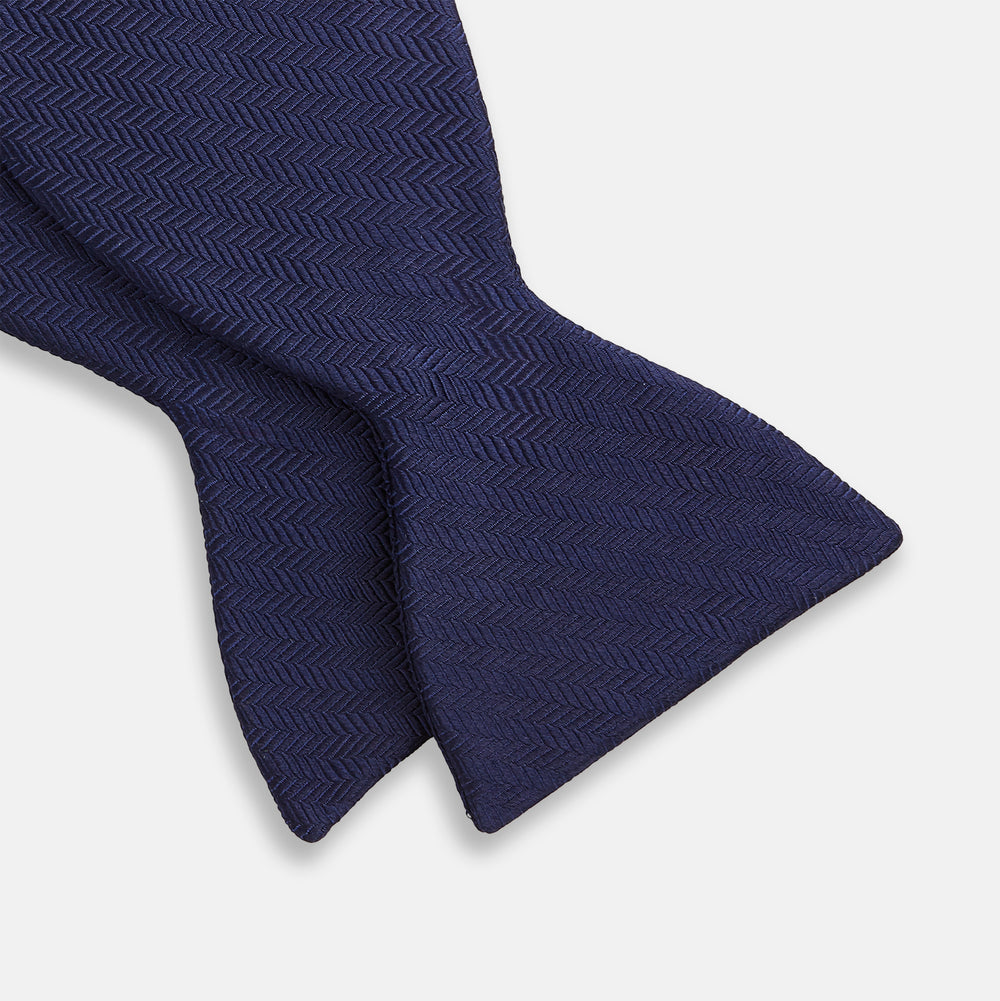 The Turnbull & Asser HERRINGBONE NAVY BOW TIE features a subtle herringbone pattern in navy blue, shown against a plain white background—the perfect accessory to elevate any smart look.