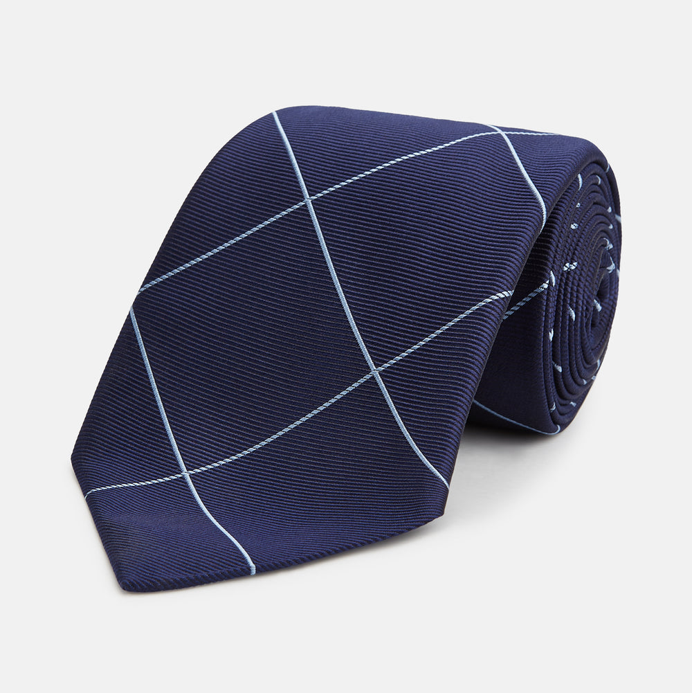 The Turnbull & Asser WINDOW PANE NAVY RIVER TIE features a navy blue base with a subtle light blue check pattern, elegantly rolled on a white background—a sophisticated men's accessory for any wardrobe.