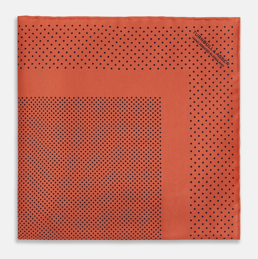 The Orange Dot Silk Pocket Square by Turnbull & Asser is handmade in England from silk, featuring small black polka dots and a solid orange border with a folded corner.