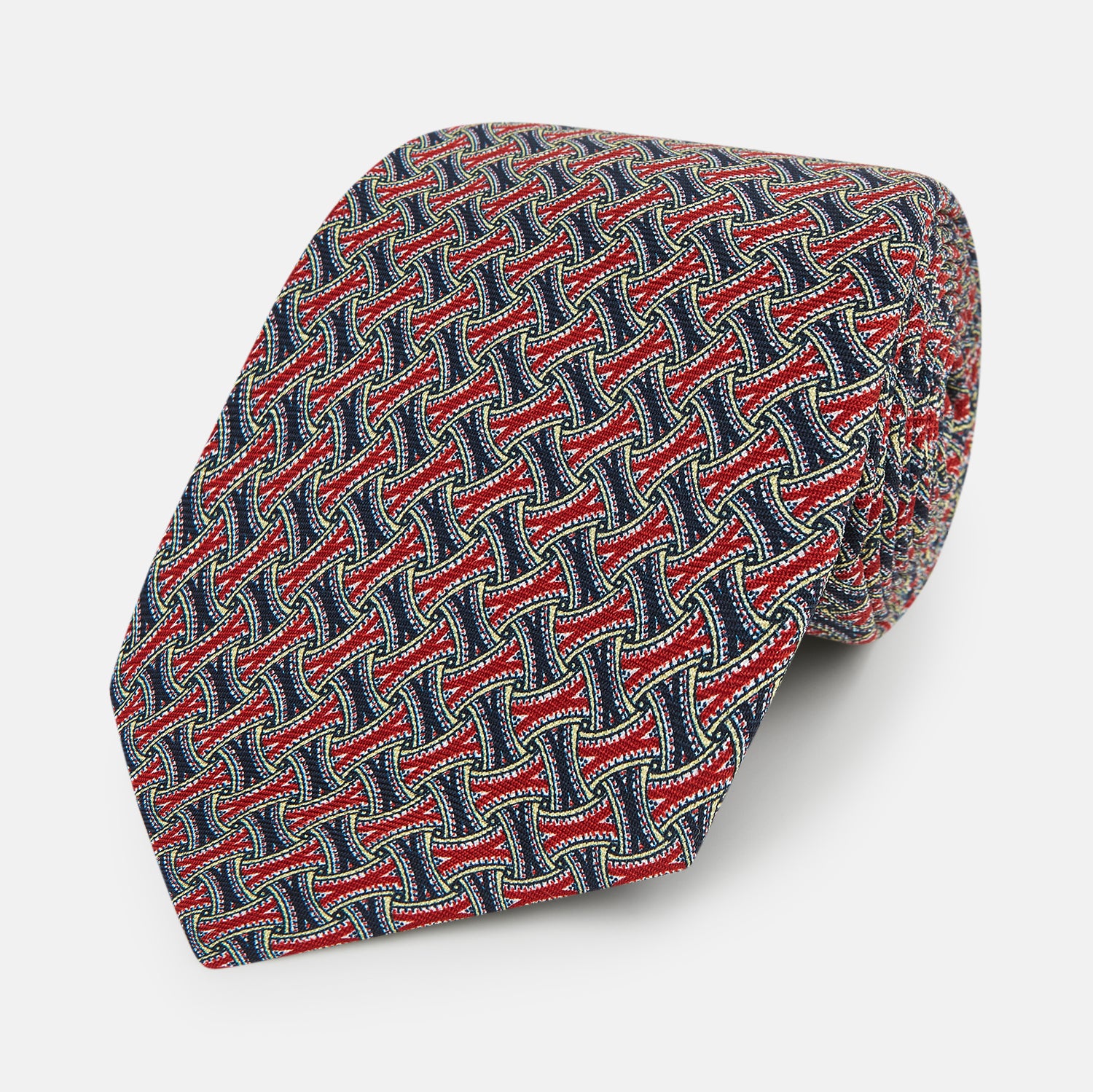 View 1 of product The Turnbull & Asser Red and Navy Weave-Patterned Printed Silk Tie features an intricate geometric design in red, blue, and white. Displayed rolled-up against a plain white background, this classic tie is crafted from luxurious silk.