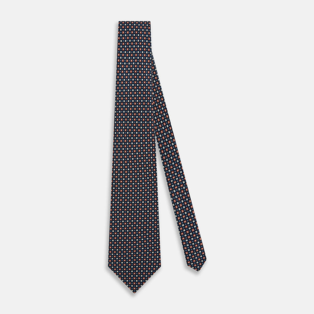 The Turnbull & Asser Navy and Orange Geometric Motif Silk Tie features a dark blue base with small orange, white, and light blue geometric patterns—a refined statement of British craftsmanship.