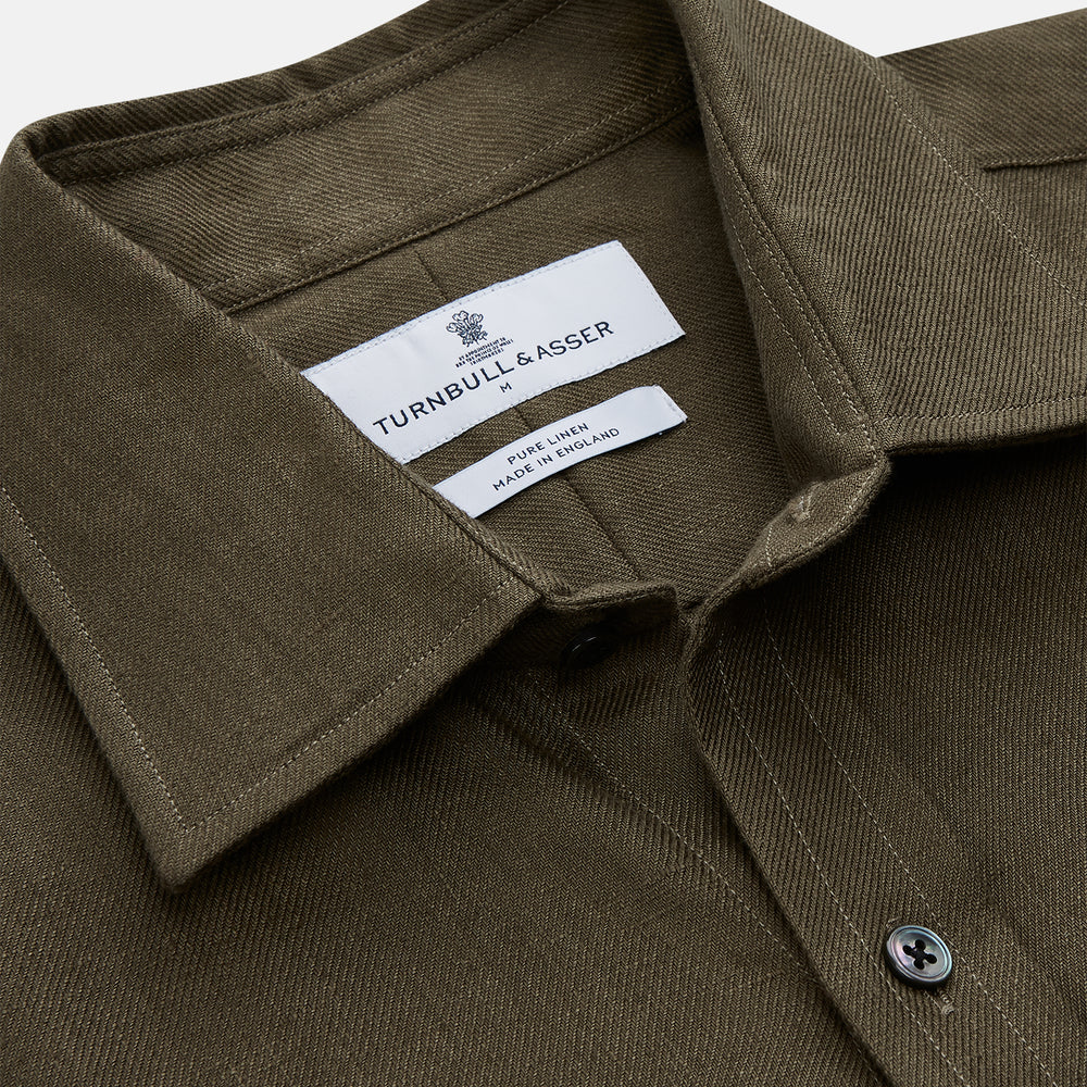 The Turnbull & Asser Khaki Green Linen Weekend Fit Langston Shirt features long sleeves, a classic Derby collar, two chest pockets, and buttoned cuffs, shown against a white background.