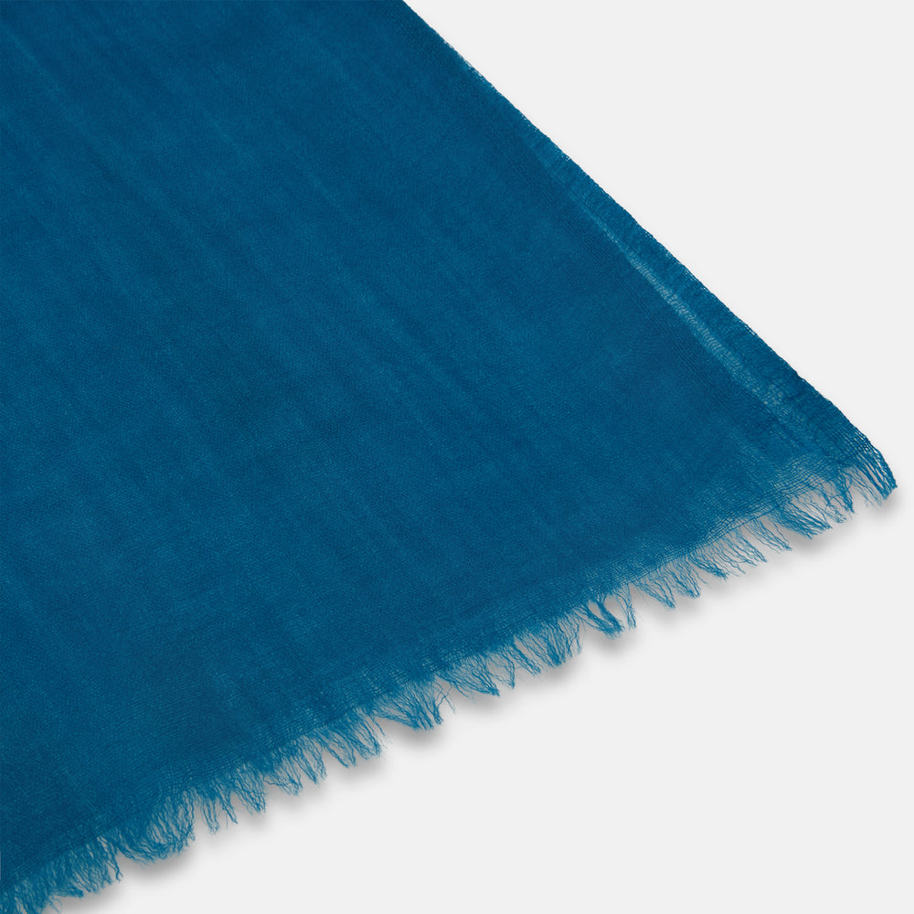 The Turnbull & Asser Steel Blue Cashmere Scarf, featuring a soft texture and slightly frayed edges, is neatly folded and tied in a loose knot against a white background.