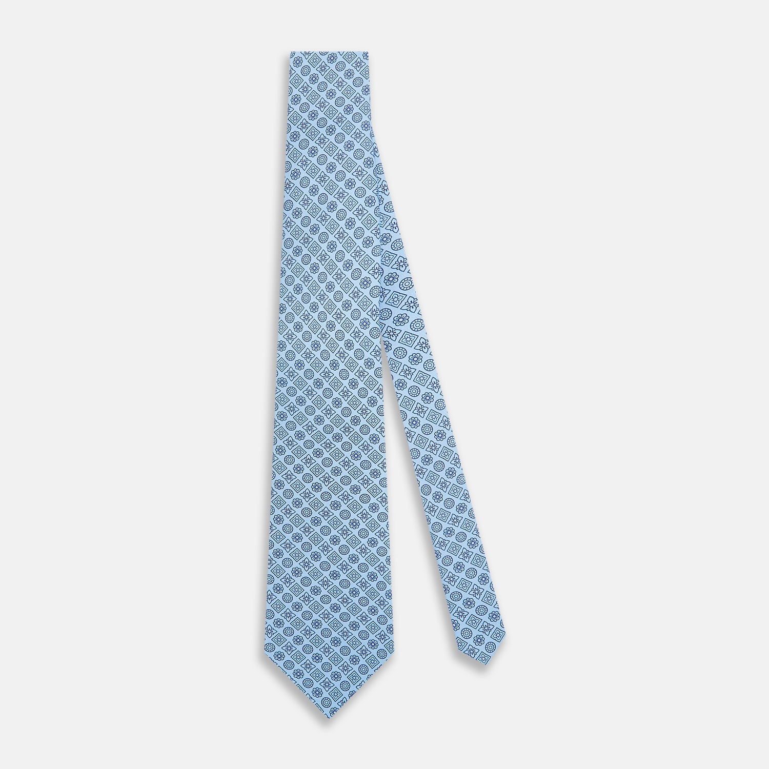 View 2 of product The Turnbull & Asser Blue Floral Tile Pattern Printed Silk Tie features a light blue geometric and floral design in dark blue, shown rolled up on a white background.