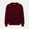 View 1 of product The Turnbull & Asser Burgundy Cashmere Cardigan features a V-neck, ribbed cuffs and hem, two front pockets, and a classic button-up design, shown on a plain white background.
