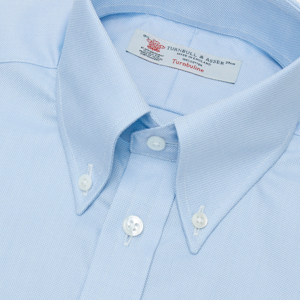 The Turnbull & Asser Light Blue Royal Oxford Cotton Shirt features a button-down collar, 3-button cuffs, and white buttons. Neatly folded with a visible inner label, it’s ideal to pair with a navy suit and displayed on a plain white background.