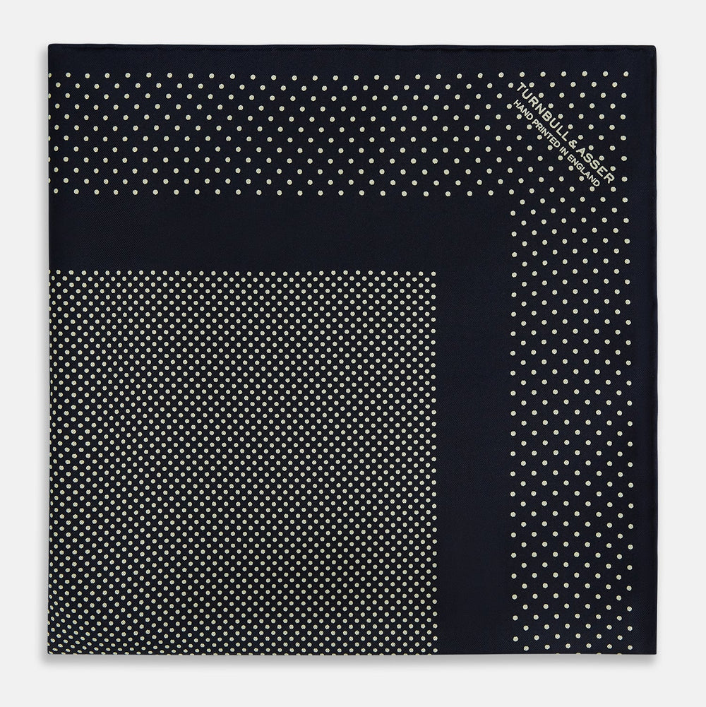 The Turnbull & Asser Navy and Cream Dot Silk Pocket Square features small cream dots, a border design, and displays handmade craftsmanship with one corner folded to show the reverse side.