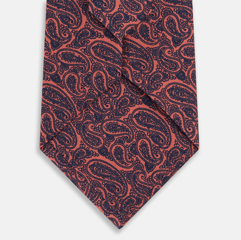 The Turnbull & Asser Orange Paisley Silk Tie, crafted from fine English silk, features an elegant paisley pattern and is stylishly rolled up on a plain white background.