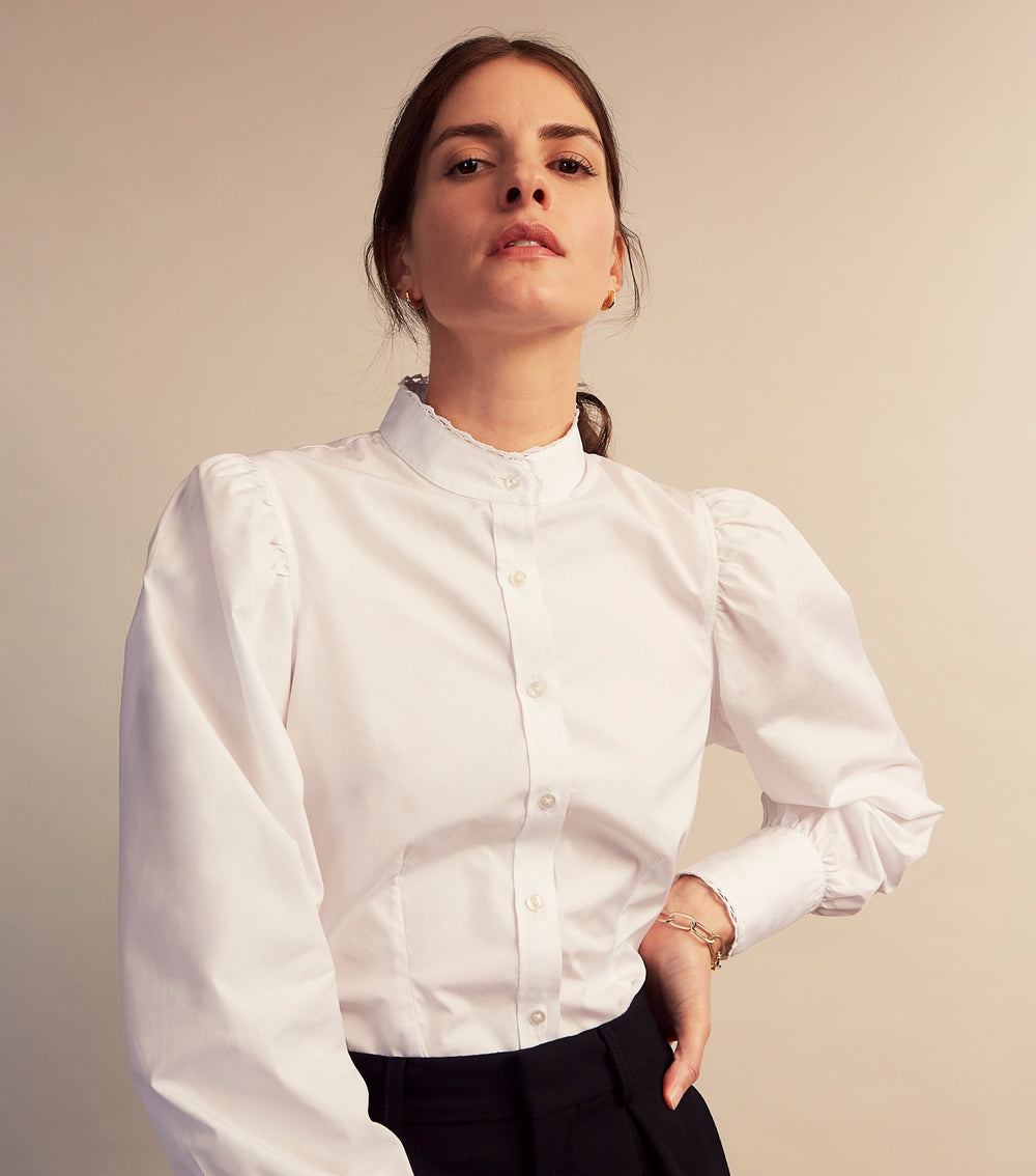 A woman stands in profile, looking down with hands in her pockets, wearing the Turnbull & Asser Turnbull and The Deck White Cotton Expressionist Shirt, paired with high-waisted black-and-white houndstooth pants.