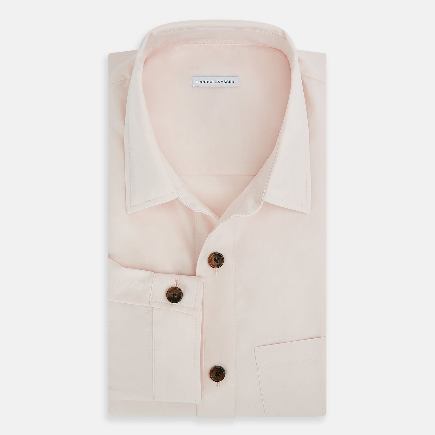 View 5 of product The Turnbull & Asser Pale Pink Hyde Overshirt is a long-sleeve, sanforised cotton button-up with a left chest pocket and dark buttons, shown laid flat on a white background.