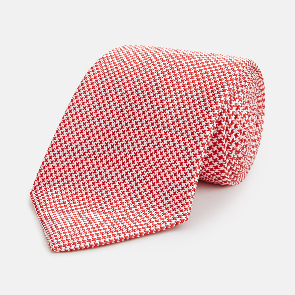 The Turnbull & Asser Red Houndstooth Silk Tie features a textured, small geometric pattern in red and white—ideal as a classic office accessory, shown rolled up on a plain white background.