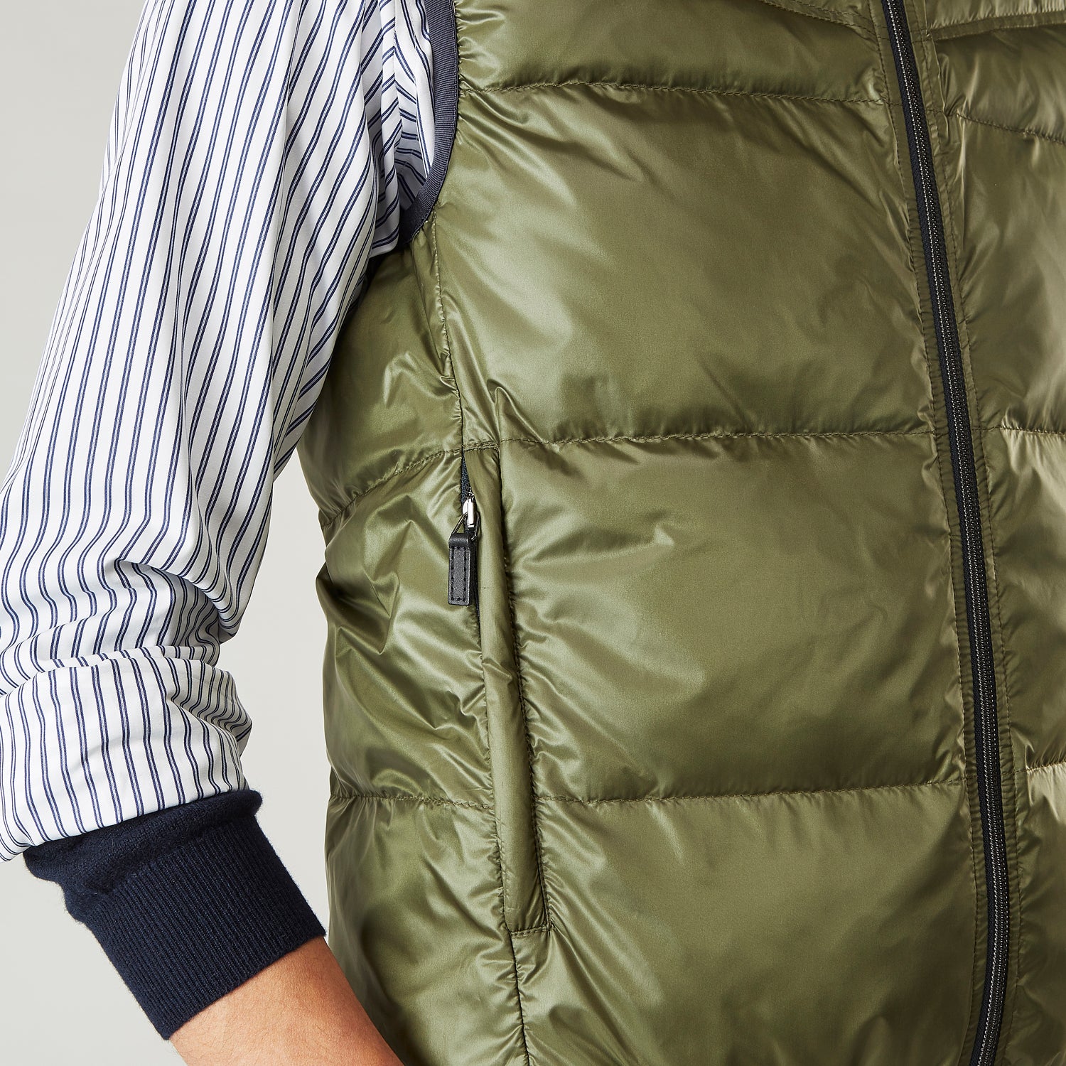 View 5 of product A man stands against a plain background wearing the Turnbull & Asser Green Peyton Sealup Quilted Gilet over a striped shirt, dark trousers, and white sneakers, with his hands in his pockets and looking slightly to the side.