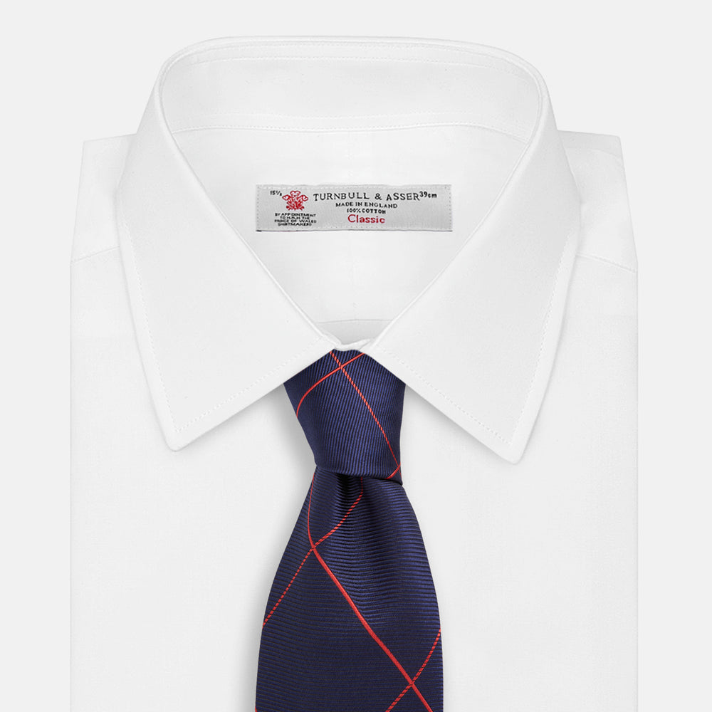 The Turnbull & Asser Red and Navy Window Pane Silk Tie features a refined diagonal red pattern on navy silk, making it an elegant choice for office attire.