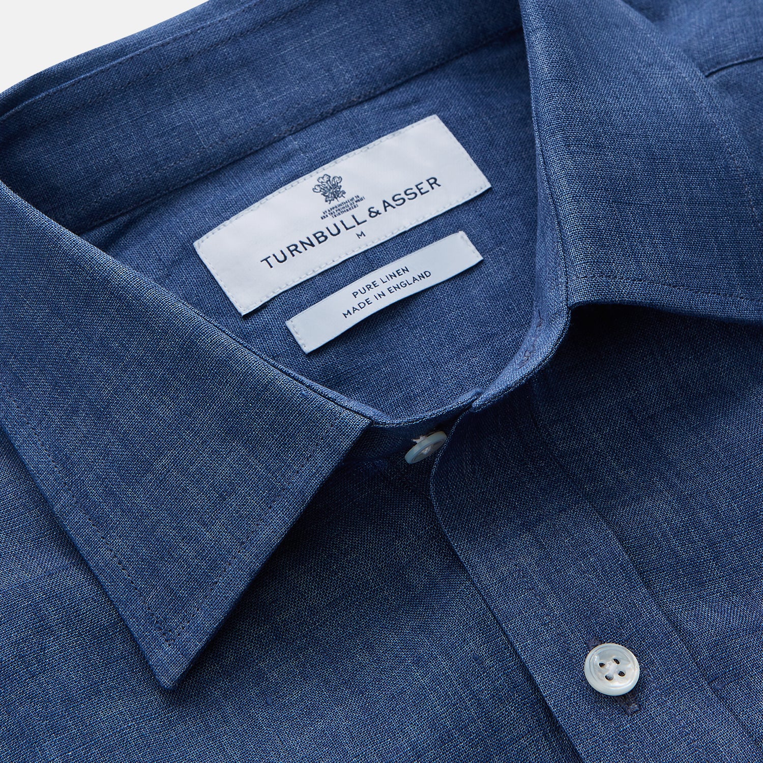 View 2 of product The Blue Weekend Fit Linen Finch Shirt by Turnbull & Asser features a Derby collar, chest pocket, and white buttons. Made from mid-blue linen chambray, it offers effortless casual style when laid flat on a plain white background.