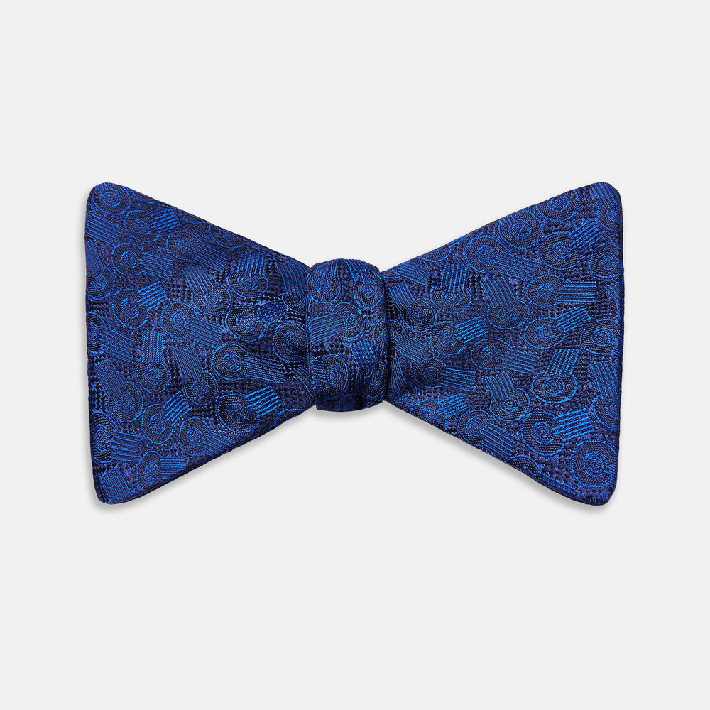 The Turnbull & Asser Electric Blue Motif Silk Bow Tie features subtle circular and swirl designs, shown on a plain white background—perfect for elevating formal attire.