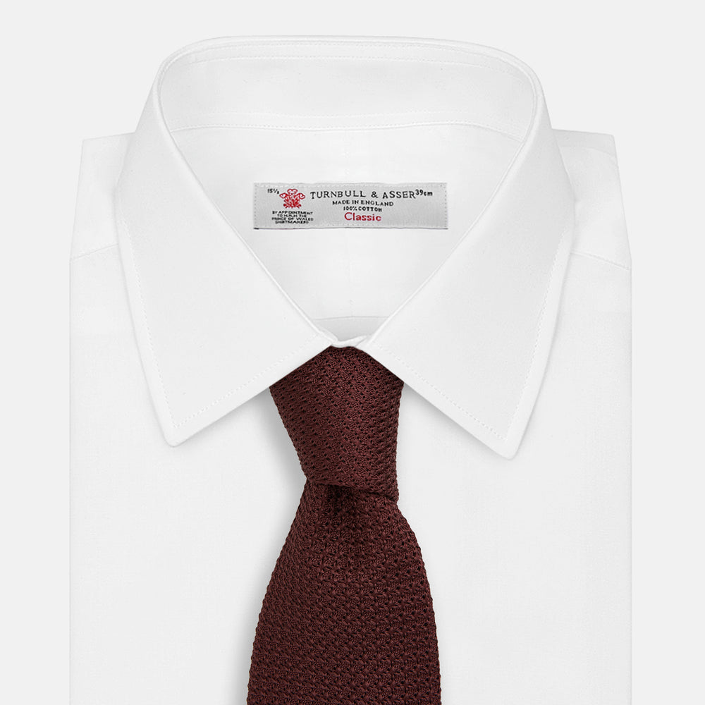 The Turnbull & Asser Burgundy Knitted Tie, rolled and featuring a textured pattern, is displayed on a plain white background—a refined accessory ideal for the modern gentleman’s wardrobe.