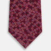 View 3 of product The Turnbull & Asser Pink and Navy Circle Burgundy Printed Silk Tie features overlapping circles in white, light blue, gold, and dark red, presented rolled up on a white background.