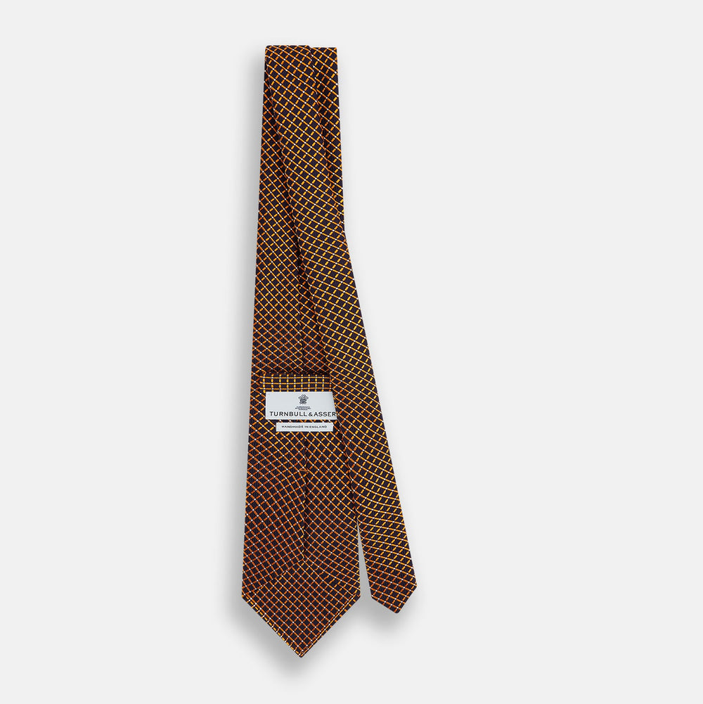 The Turnbull & Asser Orange and Navy Diamond Silk Tie features a yellow and orange diamond pattern on navy silk, ideal for modern office attire, and is displayed rolled up on a light surface.