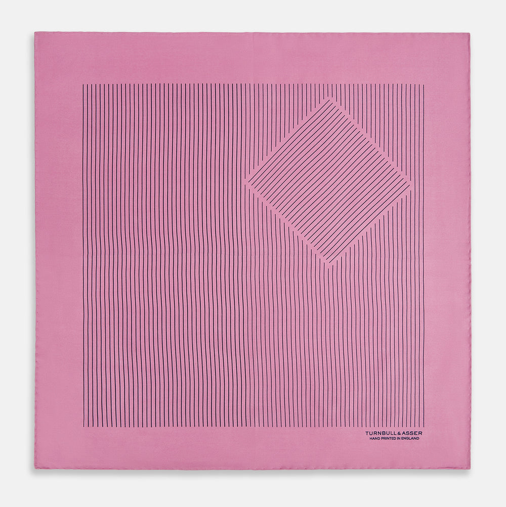 The Turnbull & Asser Pink Stripe Silk Pocket Square features thin vertical navy stripes and "TURNBULL & ASSER HAND PRINTED IN ENGLAND" in the bottom right corner, with one corner stylishly folded over.