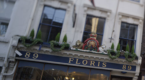 Shopfront of Floris at 89 Jermyn Street, decorated with greenery and a royal crest above the blue sign displaying the address and shop name in gold letters.