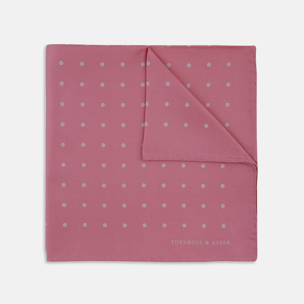 The Rose and White Spot Silk Pocket Square by Turnbull & Asser features rose pink silk with white polka dots and Turnbull & Asser branding in the corner—a refined accessory for any navy suit collection.
