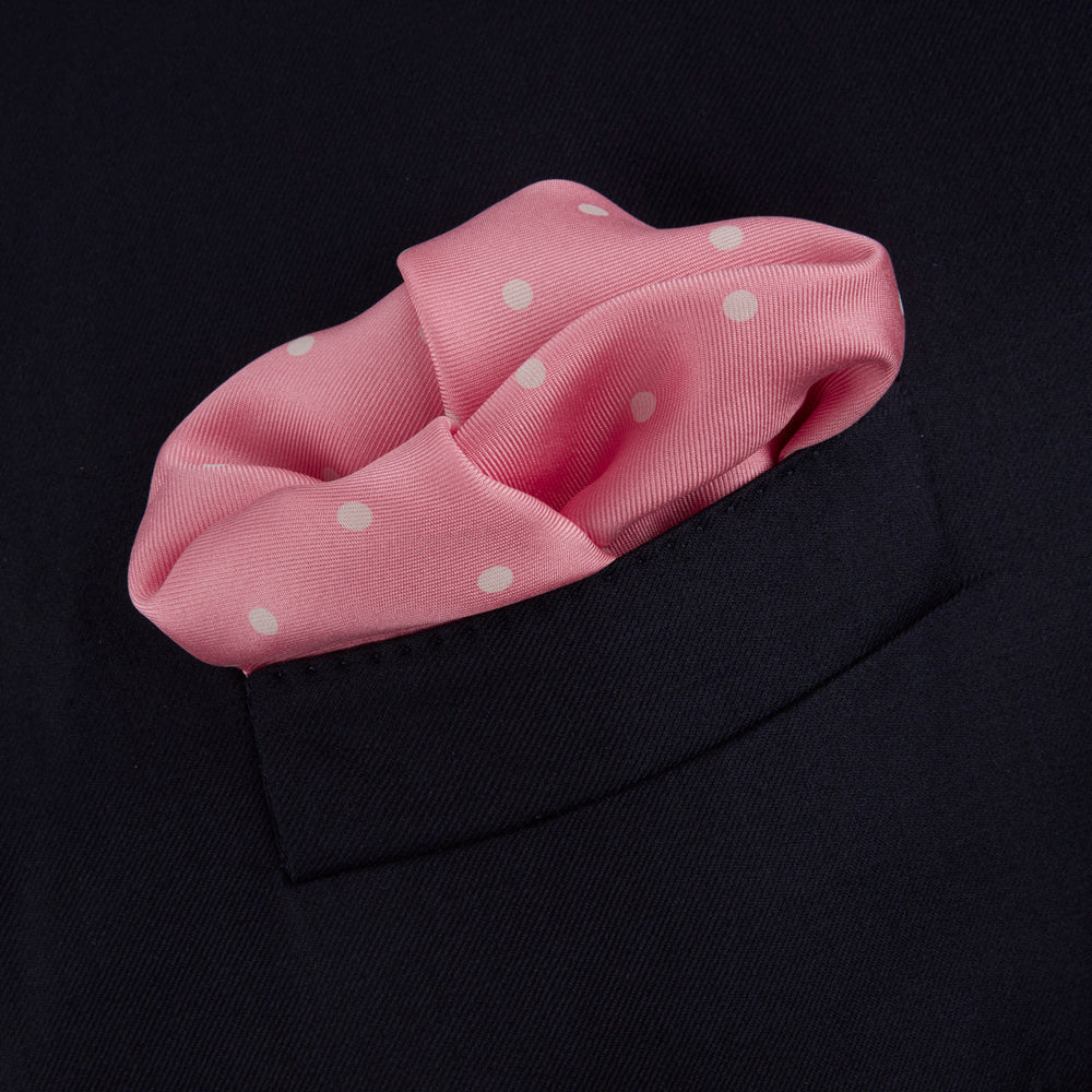 The Rose and White Spot Silk Pocket Square by Turnbull & Asser features rose pink silk with white polka dots and Turnbull & Asser branding in the corner—a refined accessory for any navy suit collection.