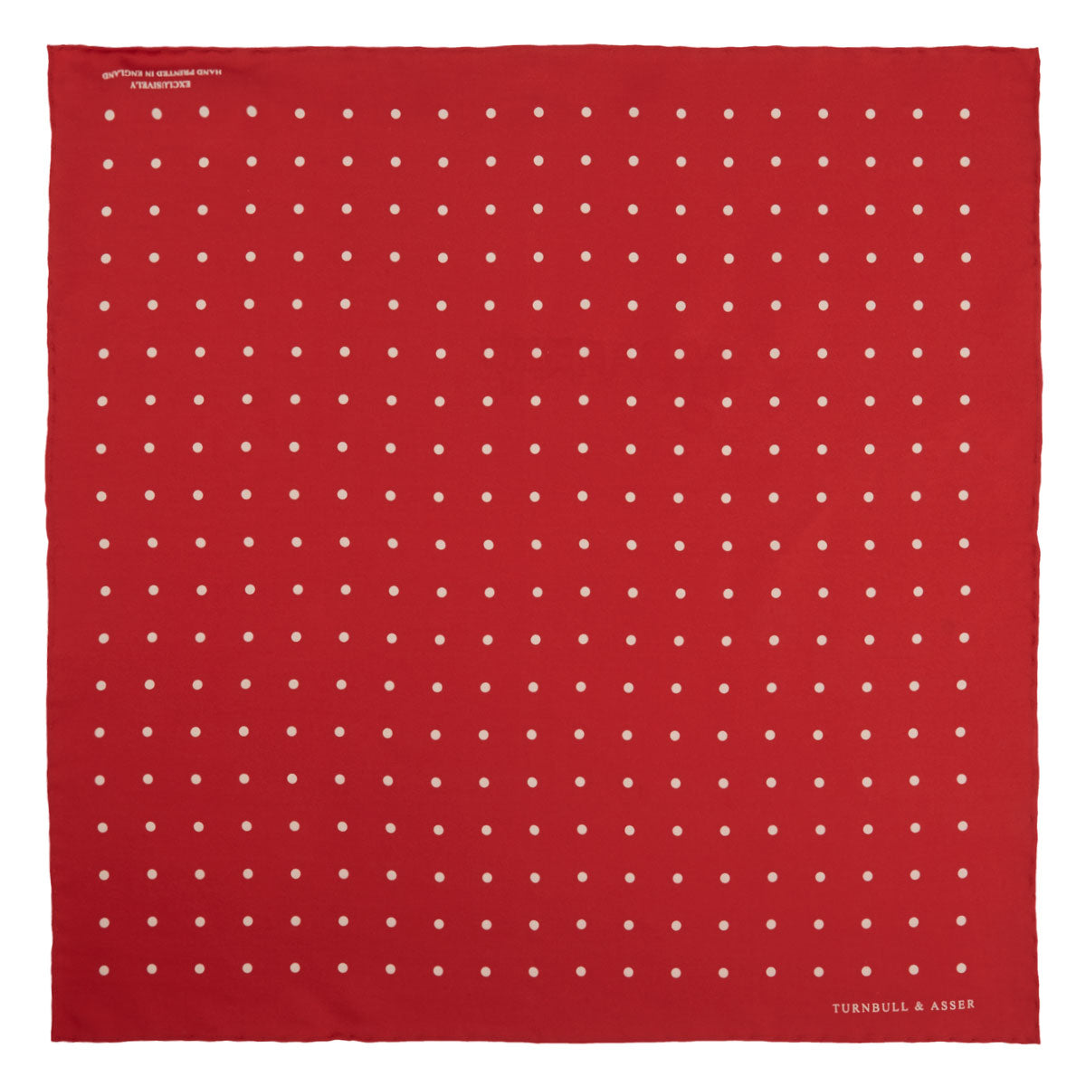 View 2 of product The Red and White Spot Silk Pocket Square by Turnbull & Asser features evenly spaced white polka dots on red silk with the brand's name printed in one corner. A folded edge reveals the reverse of this timeless pocket square.