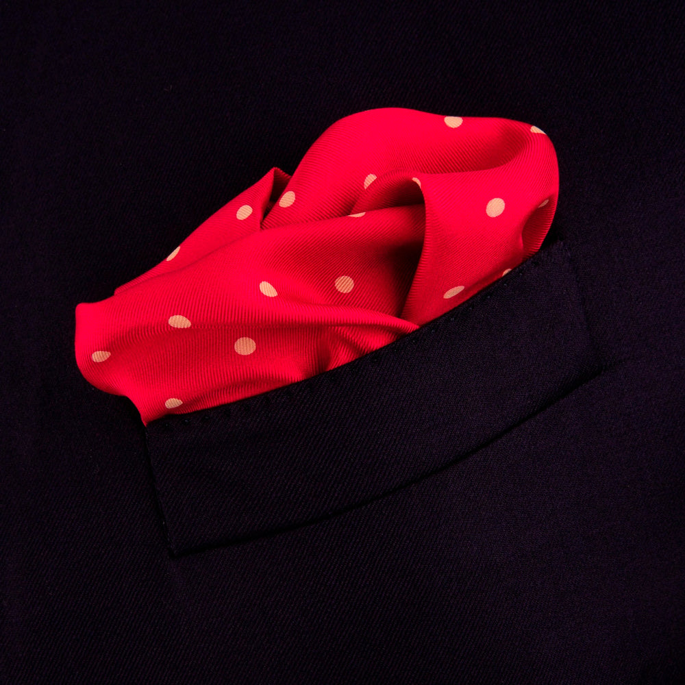 The Red and White Spot Silk Pocket Square by Turnbull & Asser features evenly spaced white polka dots on red silk with the brand's name printed in one corner. A folded edge reveals the reverse of this timeless pocket square.