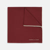 View 1 of product The Turnbull & Asser Burgundy and White Piped Silk Pocket Square features a classic burgundy design with a subtle white piped edge and the brand's logo printed in white on the bottom right corner.