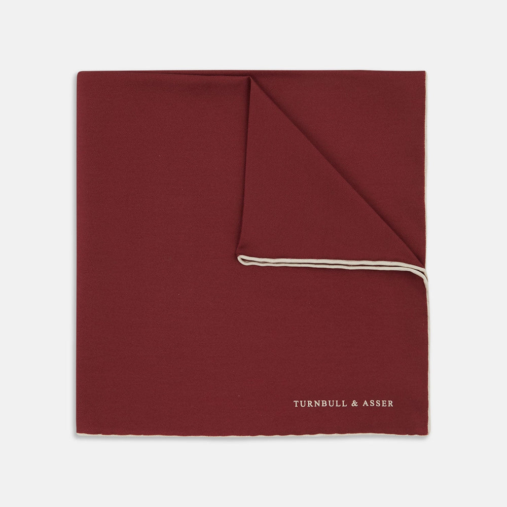 The Turnbull & Asser Burgundy and White Piped Silk Pocket Square features a classic burgundy design with a subtle white piped edge and the brand's logo printed in white on the bottom right corner.