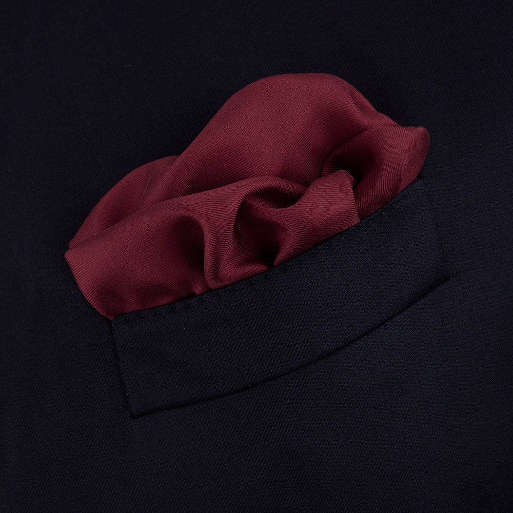 The Turnbull & Asser Burgundy and White Piped Silk Pocket Square features a classic burgundy design with a subtle white piped edge and the brand's logo printed in white on the bottom right corner.