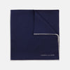 View 1 of product The Navy and White Piped Silk Pocket Square by Turnbull & Asser features white edging and partial corner folding, with the brand’s name printed in white near the lower edge.