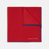 View 1 of product The Red and Navy Piped Silk Pocket Square by Turnbull & Asser features classic red silk with navy edging and the brand’s name printed in white on the bottom right corner.