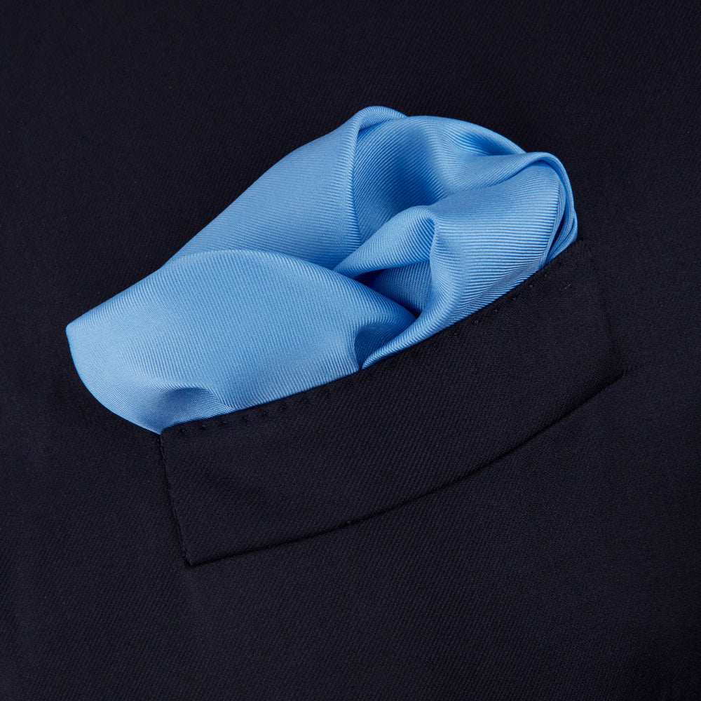 The Light Blue and Navy Piped Silk Pocket Square by Turnbull & Asser, neatly folded with dark blue edges and the brand’s white logo in the corner, is shown on a plain white background—a refined accessory for any occasion.