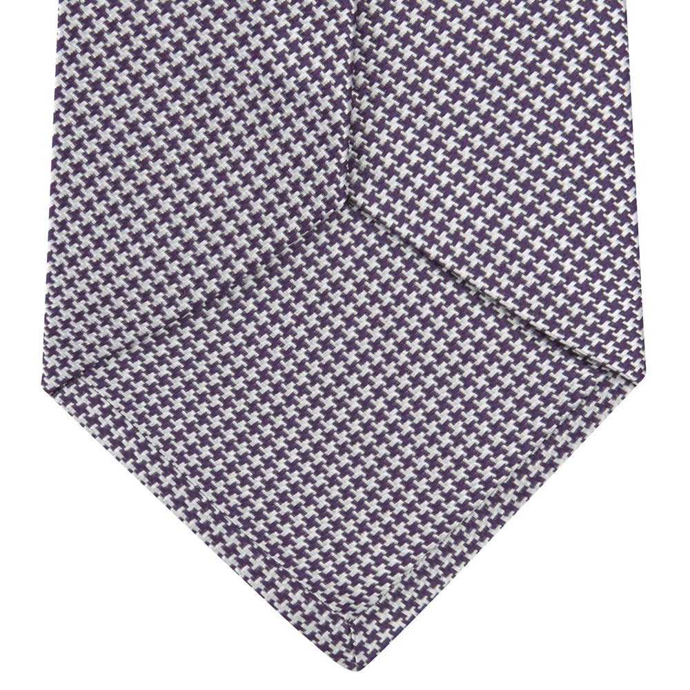The Plum Houndstooth Silk Tie by Turnbull & Asser features a refined small black, white, and gray pattern—perfect as an office shirt accessory—shown rolled up on a plain white background.