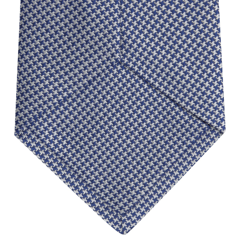 The Turnbull & Asser Blue Houndstooth Silk Tie features a classic blue and white pattern, rolled and displayed on a white background—an elegant accessory for your favorite office shirt.