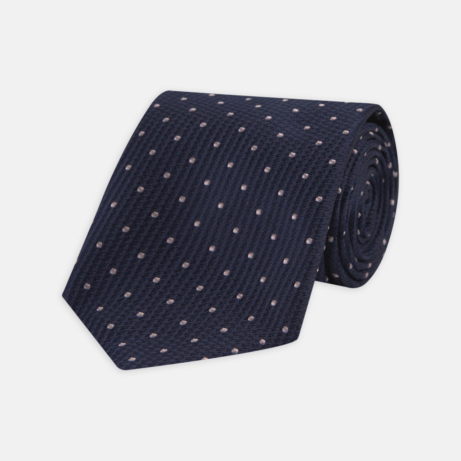 View 1 of product The Turnbull & Asser Navy and Rose Spot Lace Silk Tie features a rolled-up navy design with delicate rose spots, ideal for adding elegance to any office shirt, shown against a plain white background.